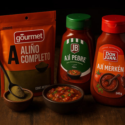 Tres condimentos chilenos (polvo de aliño completo, salsa JB Ají Pebre y salsa Don Juan Ají Merkén) dispuestos en una mesa de madera rústica con un pequeño cuenco de salsa de pebre y una minicuchara para servir, iluminados por una luz lateral de color tenue.