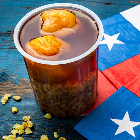 a cup of mote con huesillo on a blue table with chilean flag napkins.