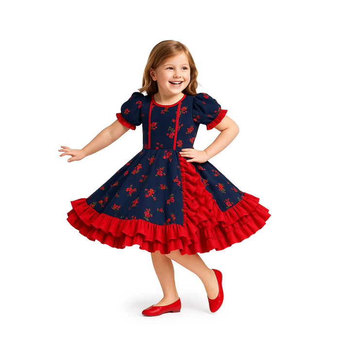 Young girl wearing a navy dress with red floral patterns and ruffles on a white background