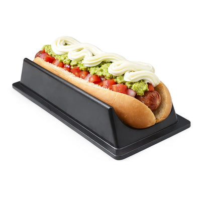 Perrito caliente con guacamole y crema agria en un soporte negro sobre fondo blanco.