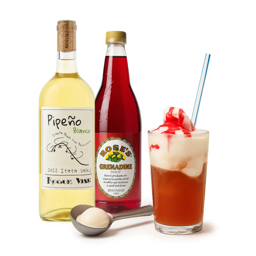 Two bottles of Pipeón Blanco and Rose's Grenadine, a glass of a red cocktail with ice cream and a straw, and a spoon with a white substance on a white background.